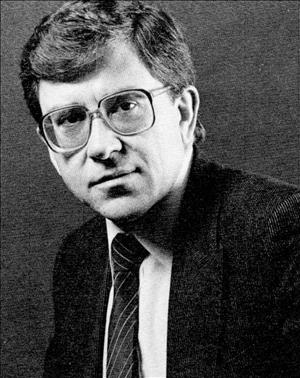 Head and shoulders portrait of a man with large, square eyeglasses and a tie. 